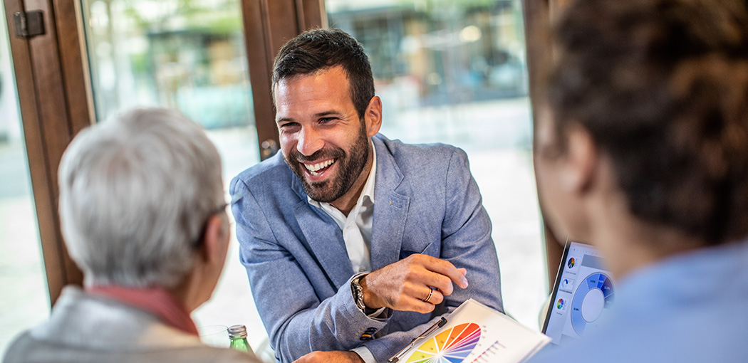 A smiling man sitting at a table talking to two other people. 